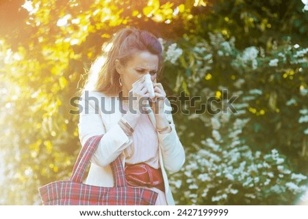 middle aged woman in pink dress and white jacket in the city with napkin and red bag has an allergy attack. Royalty-Free Stock Photo #2427199999