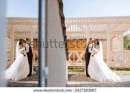 A handsome groom embraces his beloved in a beautiful location. Reflection in the mirror of the bride and groom. Wide format photo.