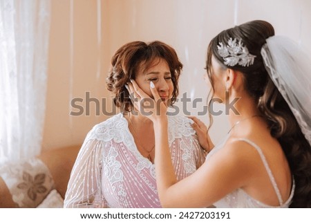 A beautiful and happy mother and her daughter, the bride, are standing next to each other. The best day for parents. Tender moments at the wedding. Royalty-Free Stock Photo #2427203191