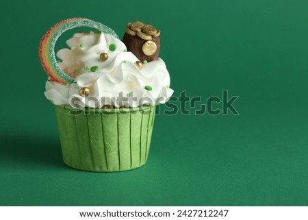 St. Patrick's day party. Tasty cupcake with sour rainbow belt and pot of gold toppers on green background, closeup. Space for text
