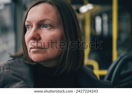 Unhappy melancholic brunette female looking out the window of public transportation shuttle bus while riding through town street, selective focus Royalty-Free Stock Photo #2427224243