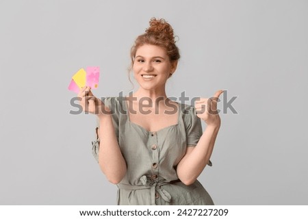 Beautiful young woman with credit cards showing thumb-up gesture on grey background