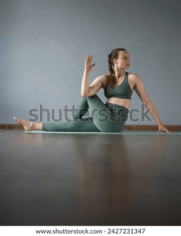 woman does stretching, yoga in gym on mat. Half fish pose. Ardha Matsyendrasana. Exercise to stretch leg muscles. Seated Twist. trainer practices asana. Gray background. Reflective floor. Side view Royalty-Free Stock Photo #2427231347
