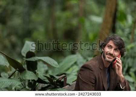 View of a young man with smartphone at daytime sitting down on a bench in a green park in the city. High quality photo.
