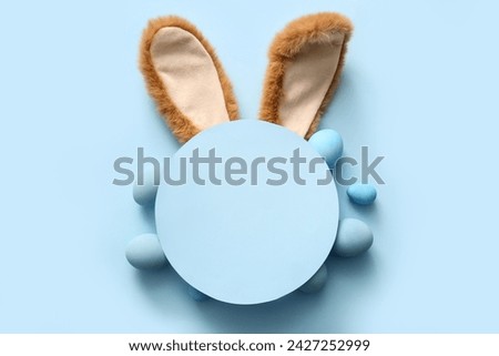 Bunny ears with Easter eggs and blank greeting card on blue background