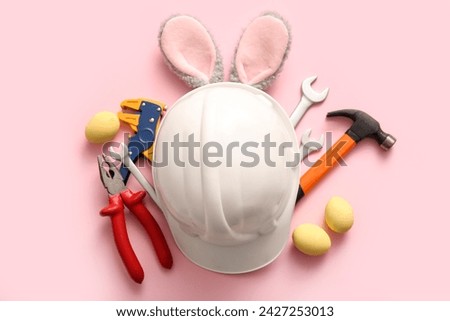 Bunny ears with Easter eggs, hardhat and construction worker tools on pink background Royalty-Free Stock Photo #2427253013