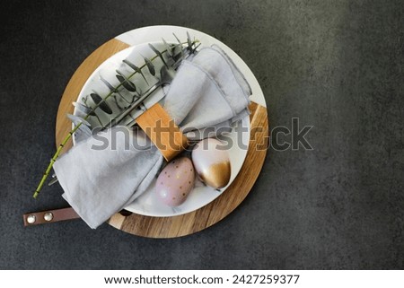 Happy Easter holiday concept. Flat lay photo of marble plate, easter eggs, cutlery and branches of eucalyptus on dark background table.