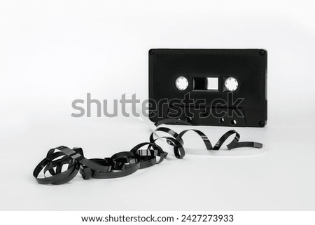 Black cassette on a white background with a tangled spiral magnetic tape from it in the foreground