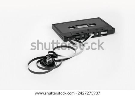 A black cassette tape lies on a white background with a tangled spiral magnetic tape in the foreground