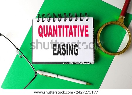 QUANTITATIVE EASING text on a notebook on green paper Royalty-Free Stock Photo #2427275197