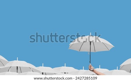 Hand holding a white umbrella high above other white umbrellas on a light blue background.