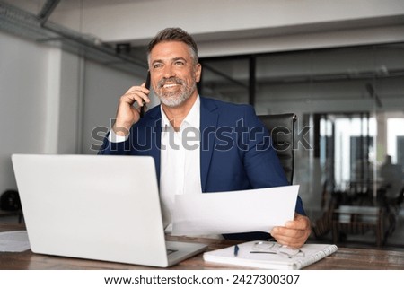 Happy smile Hispanic businessman talking phone and hear good news, checking database in office. Latin business man holding document, working at laptop computer doing online trade market tech research.