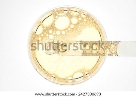 Face serum drops in a petri dish on white background. Face oil pipette dropper. Beauty facial cosmetic product texture top view. Body care lotion