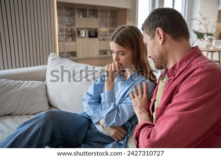 Offended wife sitting on sofa, unwilling to communicate with husband. Reserved woman is silent because of resentment, thinking about husband cheating. Caring man calming down irritated angry female Royalty-Free Stock Photo #2427310727