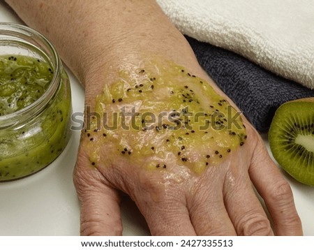 An elderly woman applies an anti-aging mask made from fresh kiwi fruit pulp to her hand