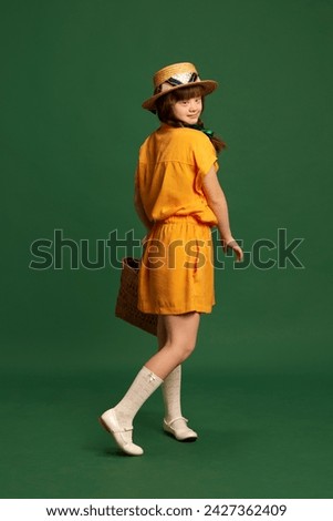 Beautiful teen girl wearing stylish yellow dress and hat standing against green studio background. Concept of childhood, emotions, fashion and lifestyle, vacation, summer