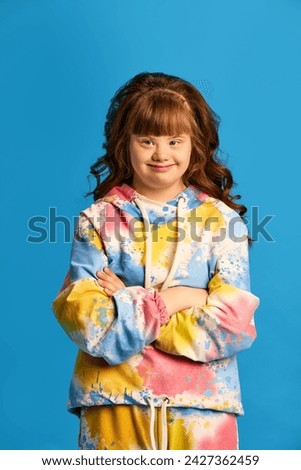 Portrait of young beautiful teen girl, wearing colorful clothes, smiling against blue studio background. Concept of childhood, emotions, fashion and lifestyle