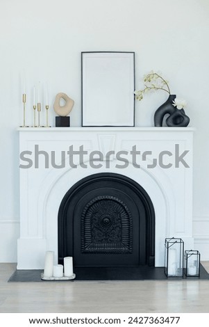 White modern decorated fireplace and mantel in interior design Scandi living room. Stylish room decorated with vase with flowers, vintage metal candlesticks with candles, picture on fireplace shelf