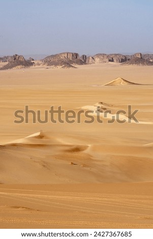 Landscape of Erg Admer in the Sahara desert, Algeria. The golden sand of Erg Admer with, in the distance, the rock formations of Tassilis. Royalty-Free Stock Photo #2427367685