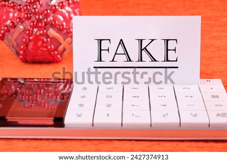 FAKE word written on a white business card on a calculator on an orange background