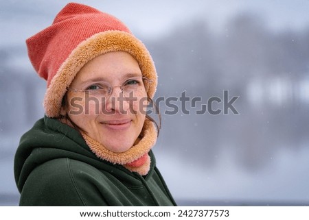 Happy woman in her early 50s outside in cold weather with light snow falling. Plenty of room for copy on the right.