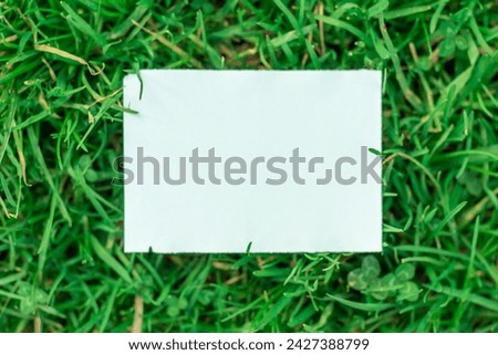 Blank paper note on green grass, top view with copy space
