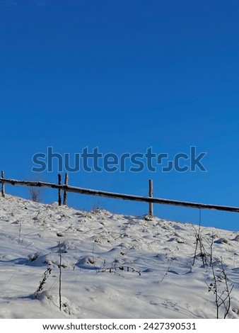 Photo of a snow-covered fence under which there is white snow against a blue sky. The photo was taken in winter on a phone in Ukraine.