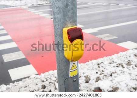 Traffic light button. Pedestrian crossing. Crosswalk yellow button. Waiting for green light. Press to change light. Winter season. Bicycle road covered with snow.