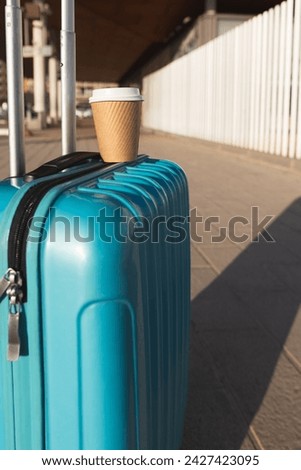 Short medium shot, single blue suitcase accompanied by a coffee machine outside the station. Travel concept.