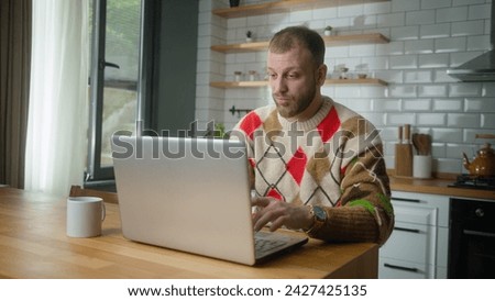 Adult man sit in the kitchen typing on laptop computer chatting with friends, enjoying surfing internet, using social media