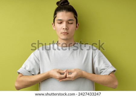 focuse guy with topknot stand meditating, keeping calm, isolated over green studio background, handsome young caucasian male with eyes closed, engaged in yoga. healthy lifestyle, people