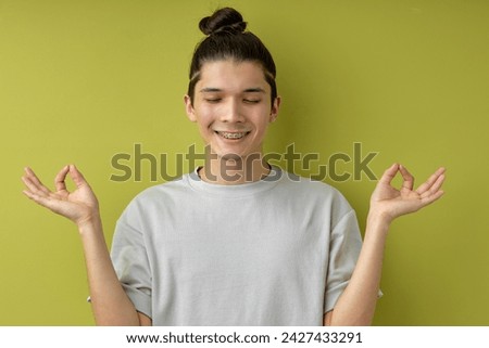concentrated guy with topknot stand meditating, keeping calm, isolated over green background, handsome caucasian male smiling with eyes closed, engaged in yoga. healthy lifestyle, people