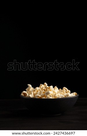 View of dark bowl with popcorn on dark table, black background, vertical, with copy space