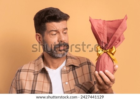 worried brazilian man looking at easter egg in beige colors. holiday, easter, celebration concept.