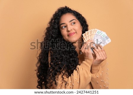 trustworthy african american woman with money, brazilian real in beige colors. financial, credit, purchase, rich concept. Royalty-Free Stock Photo #2427441251