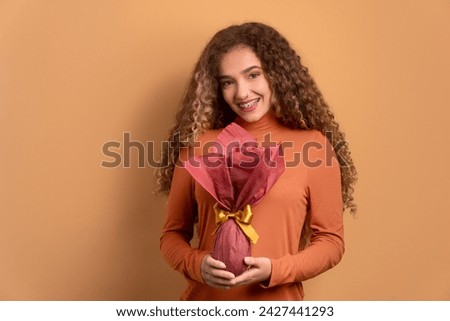 cheerful young woman showing easter egg in beige colors. holiday, easter, celebration concept. Royalty-Free Stock Photo #2427441293