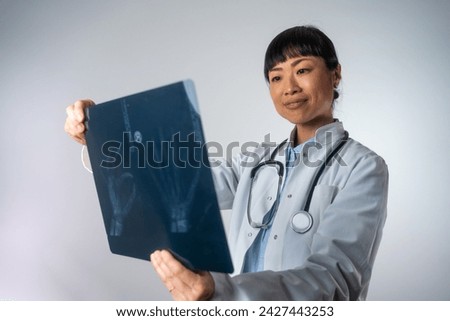 Positive Asian female doctor looking at the x-ray picture of hand in hospital. Japanese professional female doctor examining patient's x-ray of human hand during a visit