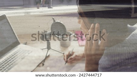 Image of biracial businesswoman recording using laptop over people and cityscape. Global business, finances, digital interface, computing and data processing concept digitally generated image.