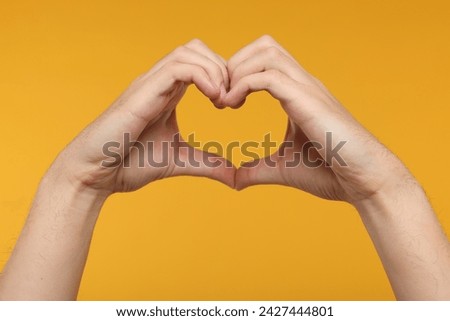 Man showing heart gesture with hands on golden background, closeup