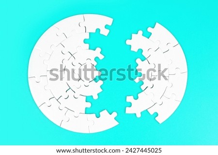 Top view of a blank circular jigsaw puzzle divided into two parts on a light blue background.