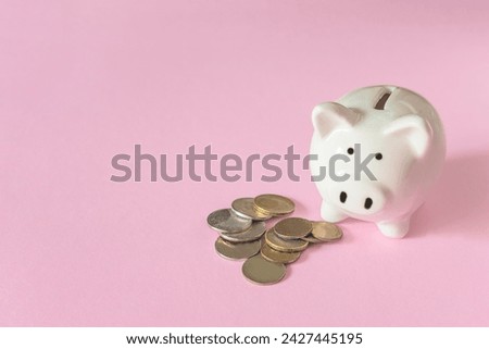White piggy bank and some monets on a pink background