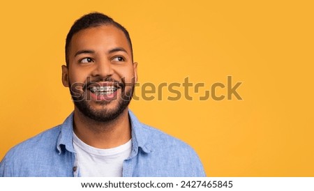 Smiling young african american man with orthodontic braces looking at copy space, happy handsome black guy exuding confidence and joy, posing on vibrant yellow background, panorama
