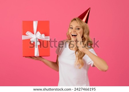 Birthday Offer. Joyful young blonde woman in festive hat holding wrapped present box and shouting with hand near mouth, announcing bday discount against pink studio background. Holiday celebration