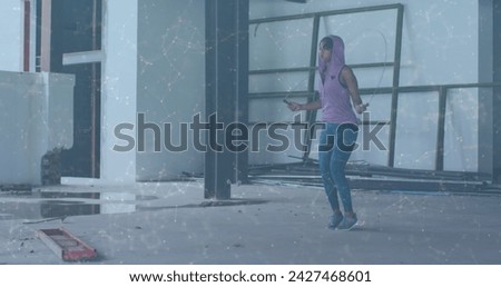 Image of network of connections over woman jumping the rope in an abandoned building. Digital interface global sport and performance concept digitallygenerated image.