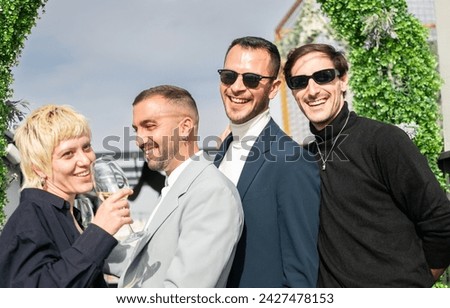 Newlywed homosexual couple laughing with friends under a mistletoe. Three men and one woman. Outdoors, with sunlight.