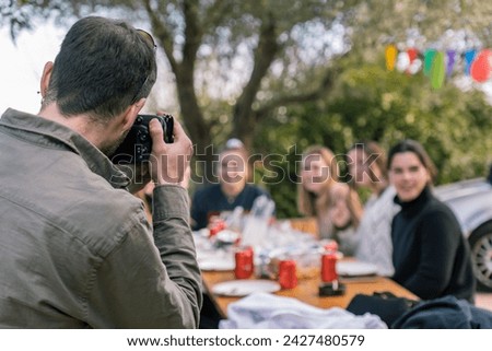 Young man taking a picture of girls sitting at the table during a birthday party with a reflex camera.