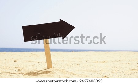 Empty wooden direction sign at the tranquil beach. Right pointing blank black direction sign. Royalty-Free Stock Photo #2427488063