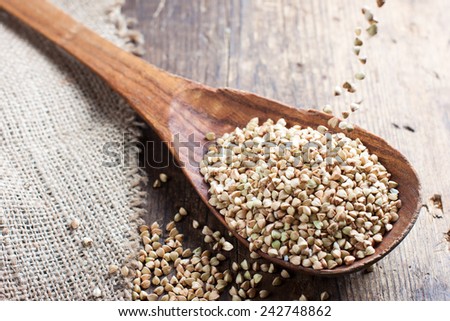 green buckwheat spilling in a wooden spoon on a background of burlap and dark old wooden table in rustic style