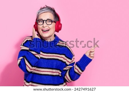 Photo of attractive pensioner woman headphones point empty space wear trendy blue striped clothes isolated on pink color background