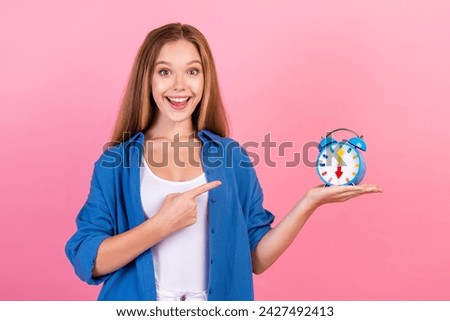 Photo of positive cheerful girl wear blue shirt pointing finger classic clock isolated pink color background